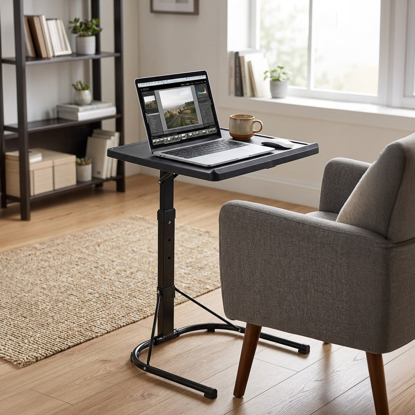 Un portátil mostrando software de edición de fotos en una mesa ajustable junto a un sillón.