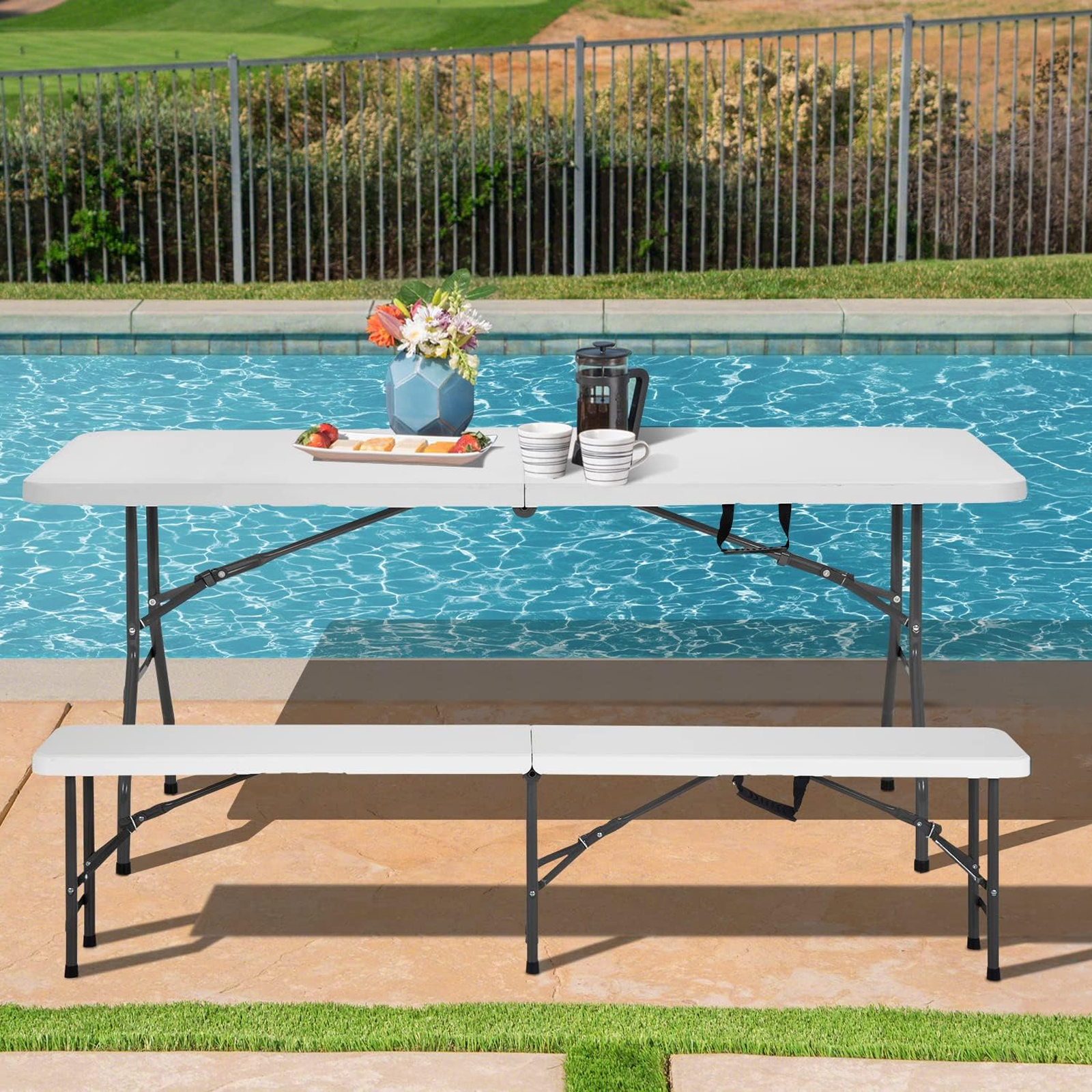 Conjunto blanco junto a la piscina: mesa con flores, fruta, café; banco al lado.