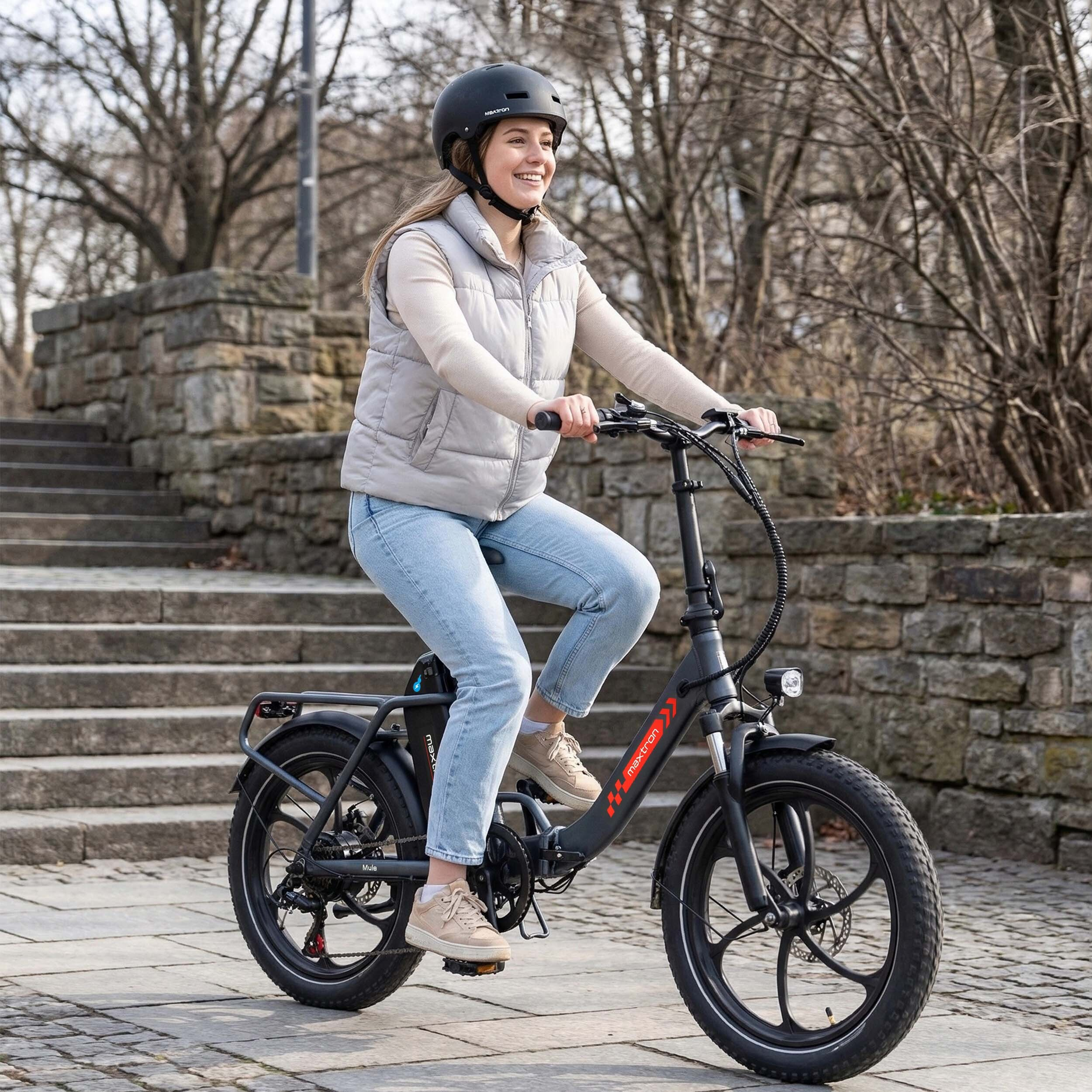 Kobieta w kasku jedzie czarnym rowerem elektrycznym po kamiennych schodach.