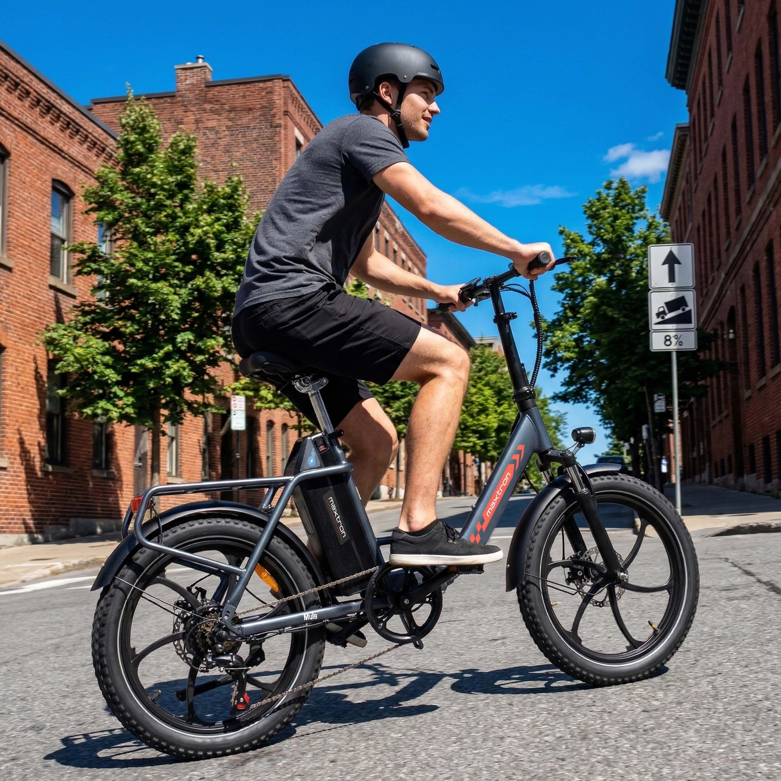 Mężczyzna jedzie rowerem elektrycznym po ulicy wyłożonej ceglanymi budynkami.