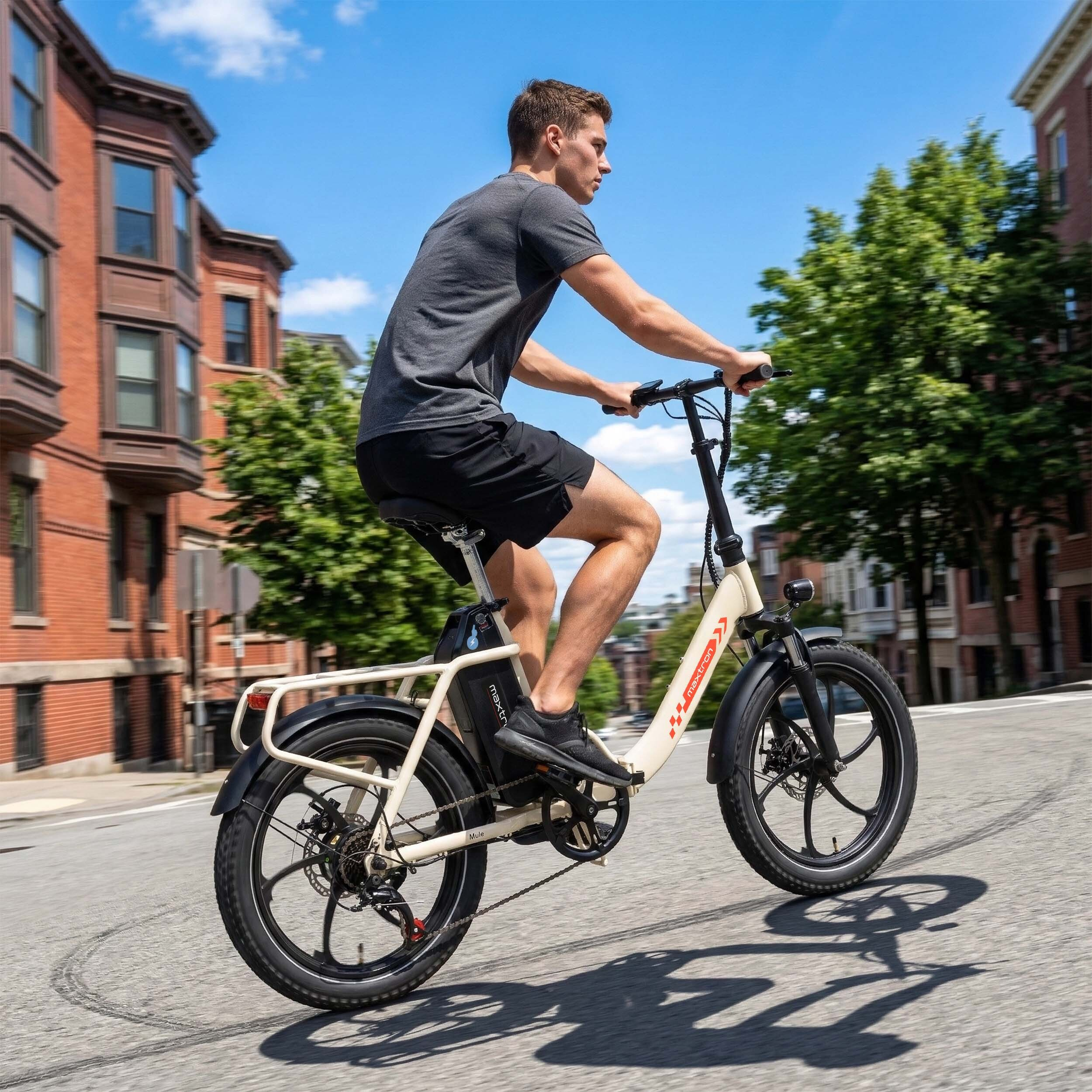 Mężczyzna jedzie kremowym rowerem elektrycznym po ulicy z ceglanymi budynkami i drzewami.