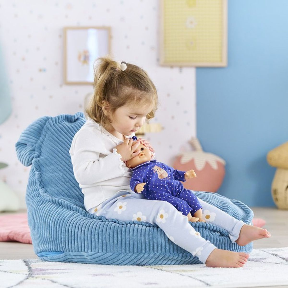 Ein kleines Mädchen sitzt auf einem blauen Sitzsack und spielt mit einer Puppe.