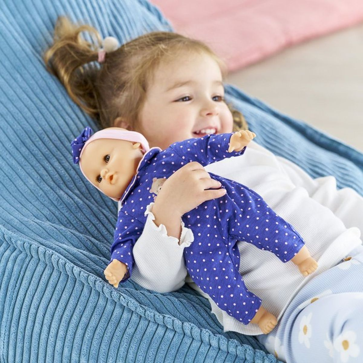 Ein kleines Mädchen hält eine Puppe in einem blauen Overall mit weißen Punkten.