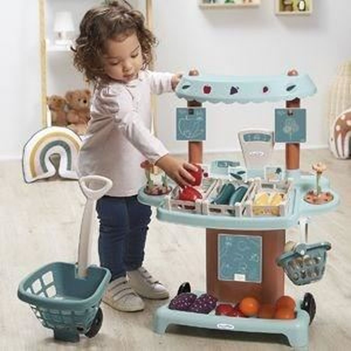 Ein kleines Mädchen spielt mit einem Spielzeug-Obststand mit einem Einkaufswagen.