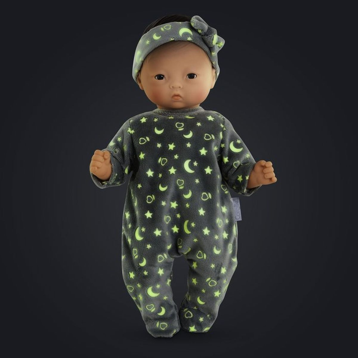 Ein Baby-Puppe in Schlafanzug mit Monden und Sternen, vor dunklem Hintergrund.