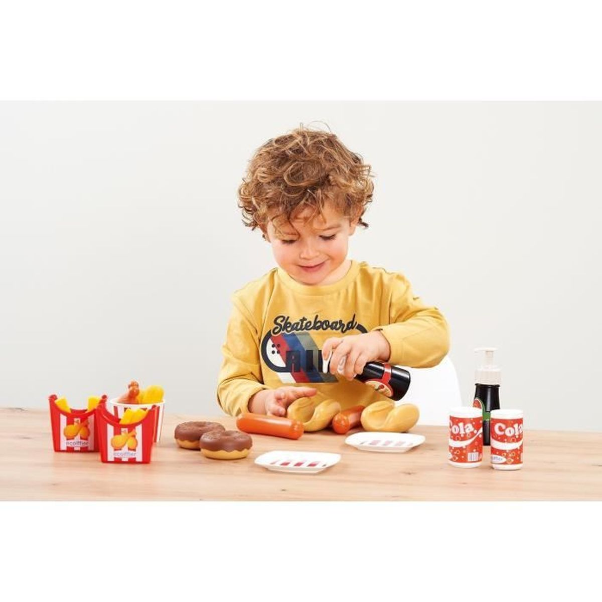 Ein Junge spielt mit Spielzeug-Fast-Food, darunter Pommes, Hotdogs und Getränke.