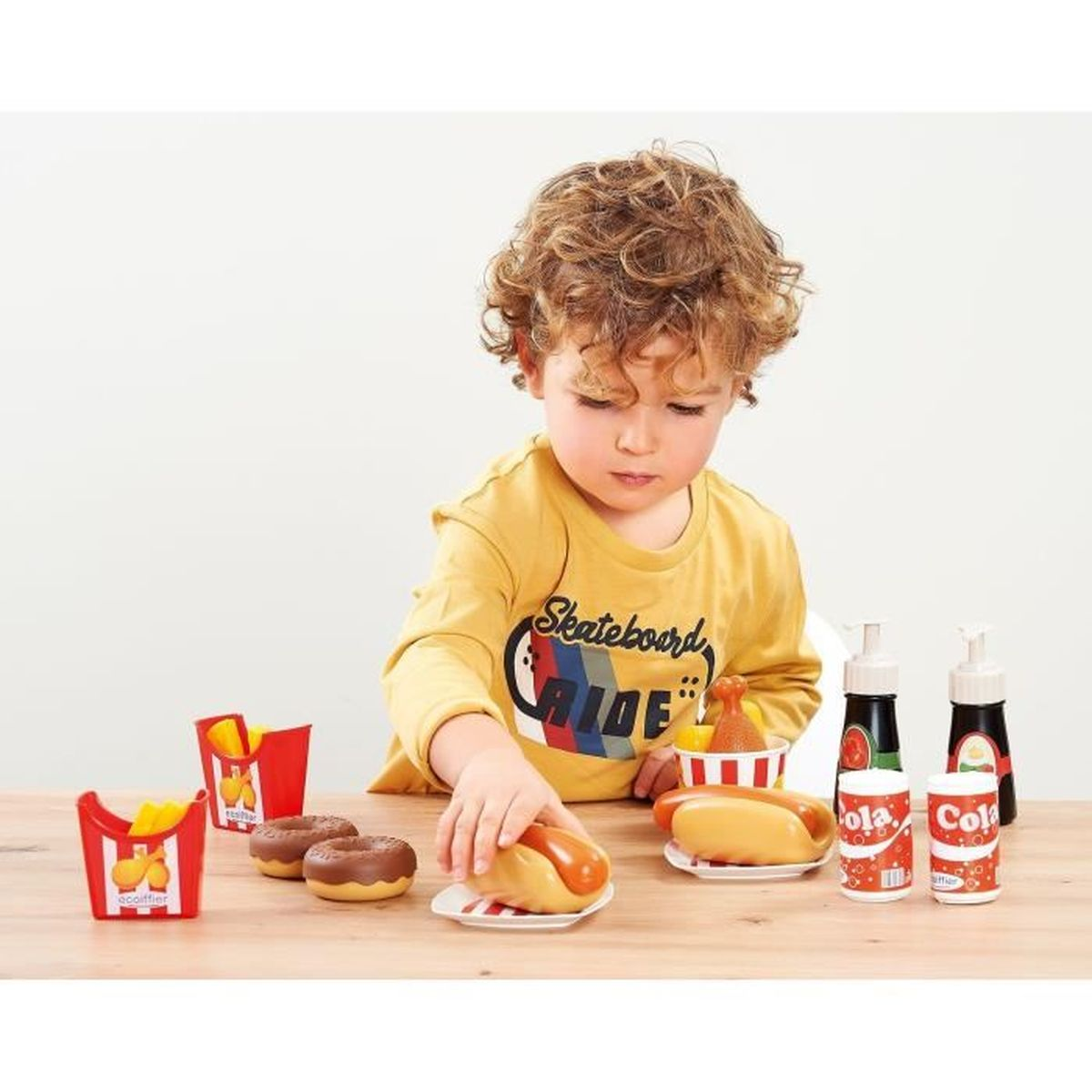 Kleiner Junge spielt mit Spielzeug-Fast-Food-Set mit Hotdog, Pommes, Donuts und Cola.