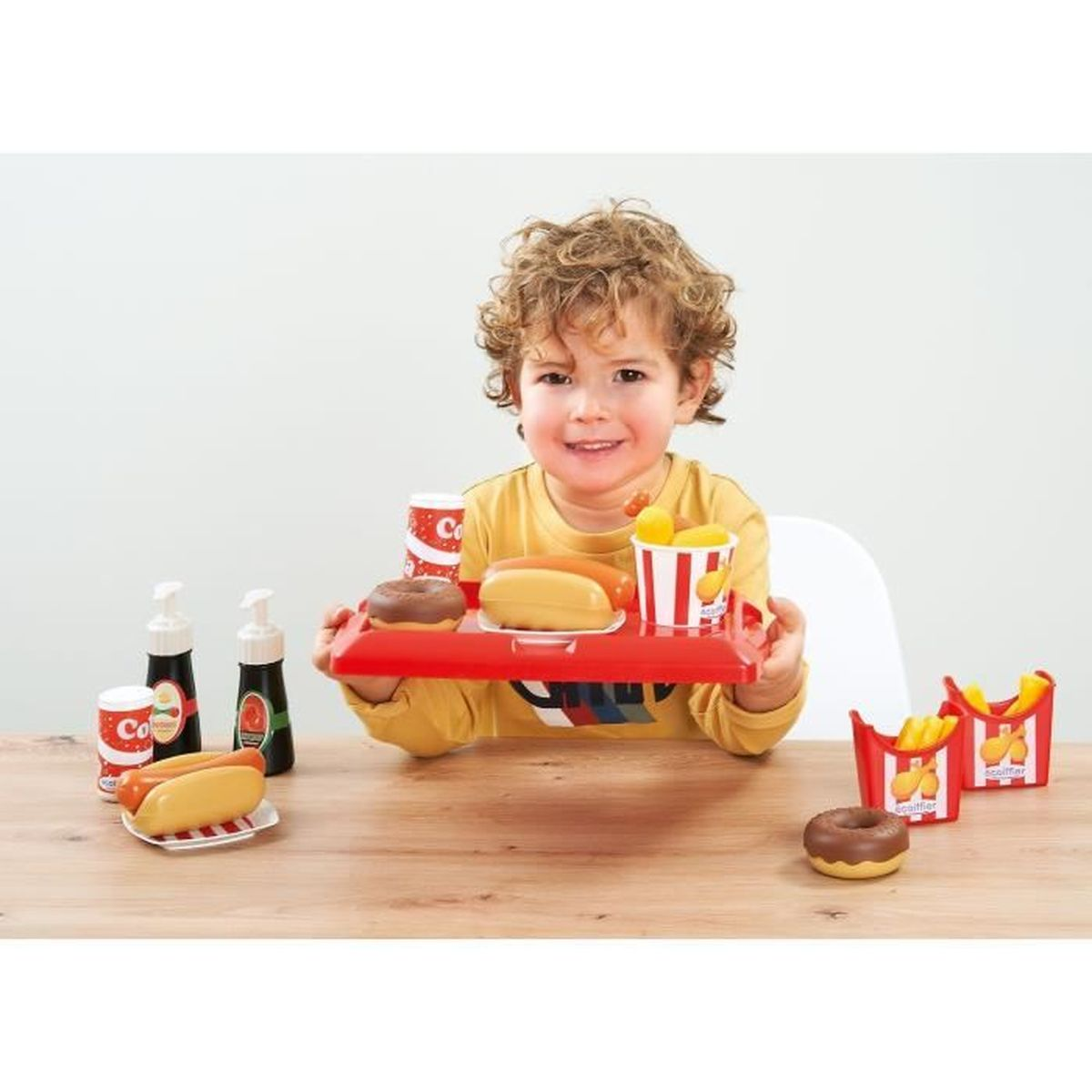 Ein Junge hält ein Tablett mit Spielzeug-Fast-Food, darunter Hotdogs und Pommes.
