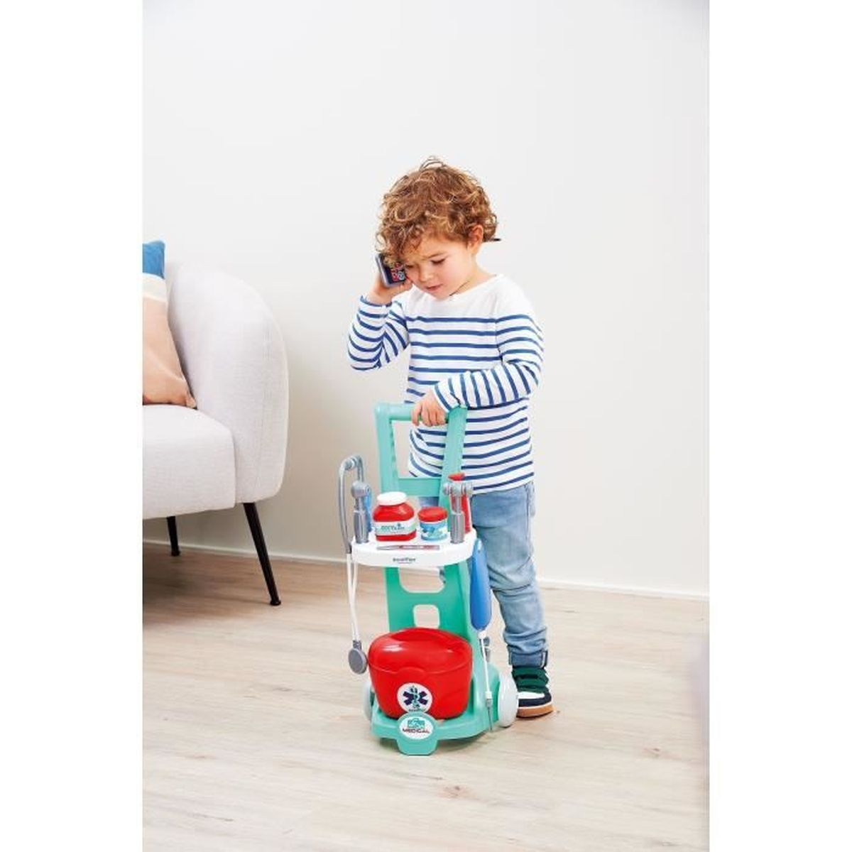 Ein kleiner Junge telefoniert neben einem Spielzeug-Arztwagen mit medizinischem Zubehör.
