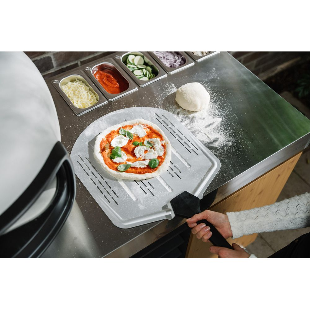 Pizza non terminée sur une pelle avec des ingrédients en arrière-plan.