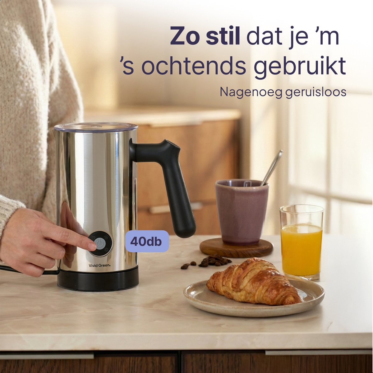 A silver milk frother with a black handle, next to a croissant.