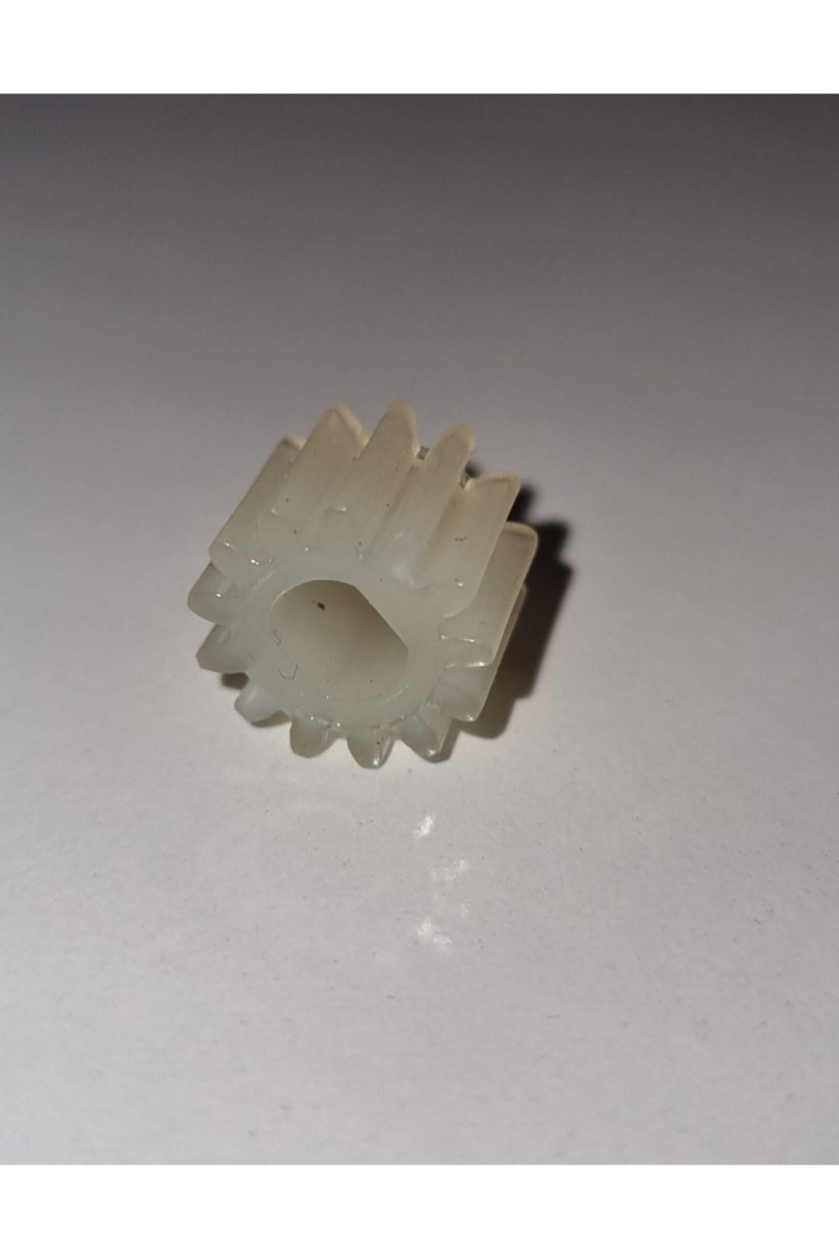 Açık gri arka plan üzerinde çok sayıda dişe sahip küçük, beyaz plastik dişli.