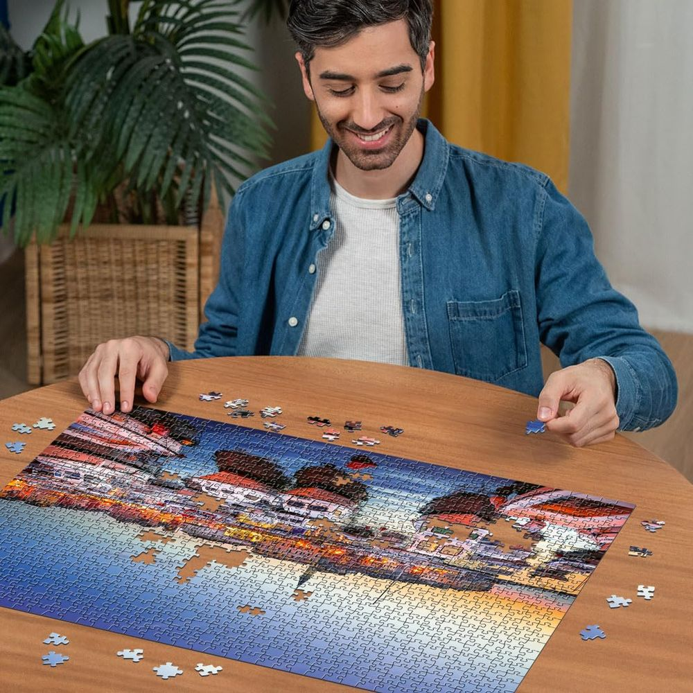 Uomo completa un puzzle di una città illuminata al tramonto.