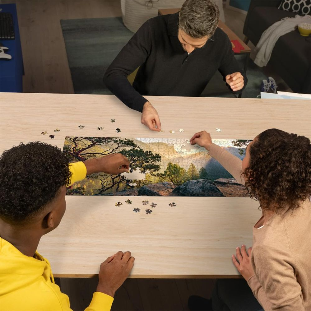 Tre persone compongono un puzzle di un paesaggio montano con alberi.