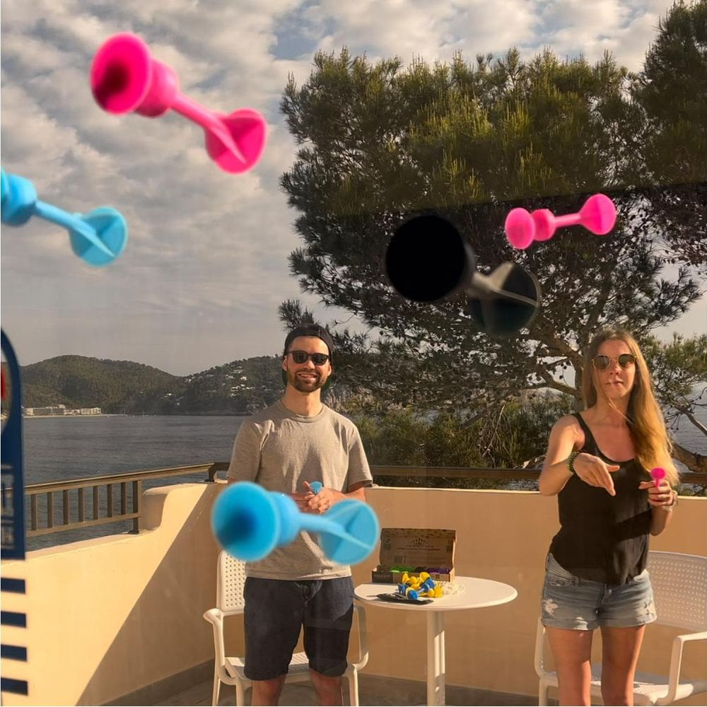 Uomo e donna su balcone lanciano giocattoli rosa e blu con ventosa. Mare e colline sullo sfondo.