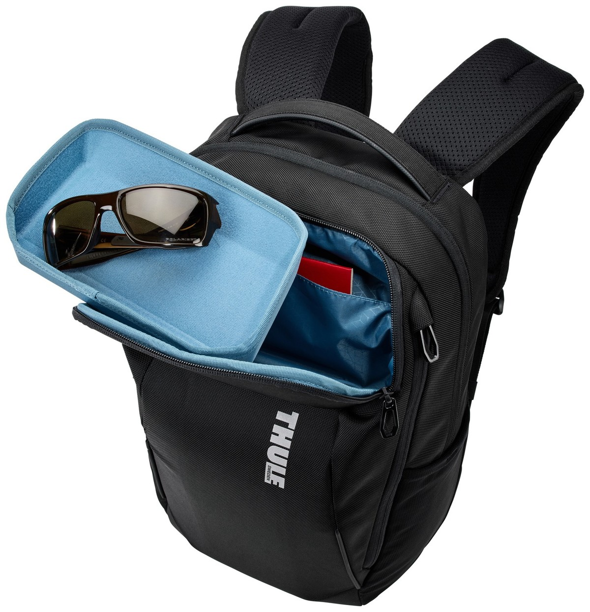 Schwarzer Rucksack mit einem blauen Fach, Sonnenbrille und rotem Buch.