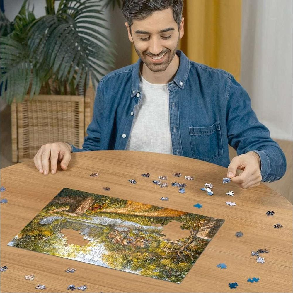 Mann puzzelt Bild eines Sees mit Bäumen und einem Haus.