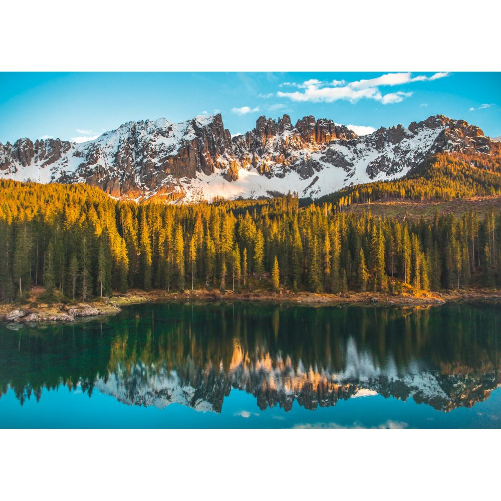 Alberi verdi si riflettono in un lago calmo davanti a montagne innevate.