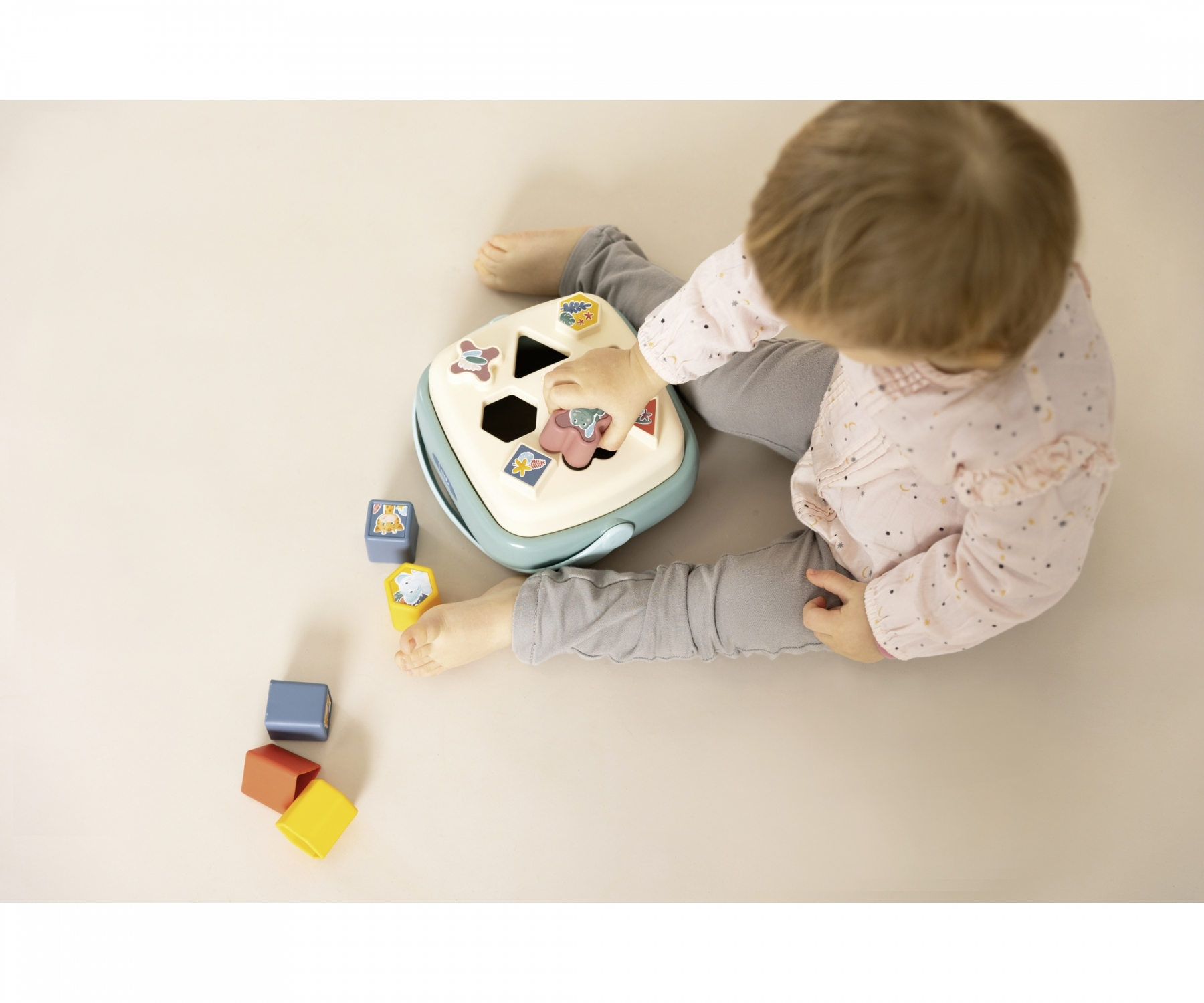 Un bambino gioca con un incastra forme e blocchi colorati su un pavimento chiaro.