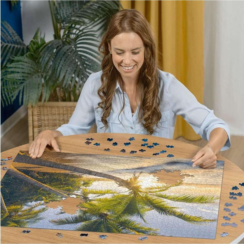 Femme assemblant un puzzle d'un coucher de soleil sur la plage avec des palmiers.