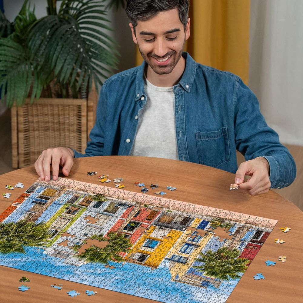 Mann baut ein Puzzle mit bunten Häusern am Wasser.