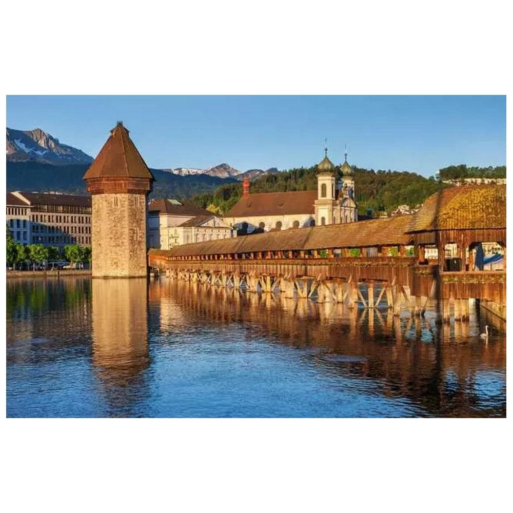 Holzbrücke über Fluss mit Turm und Bergen im Hintergrund.