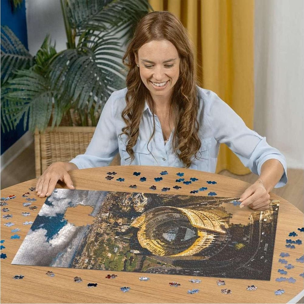 Una donna assembla un puzzle di uno stadio. Molti pezzi del puzzle sono sparsi.