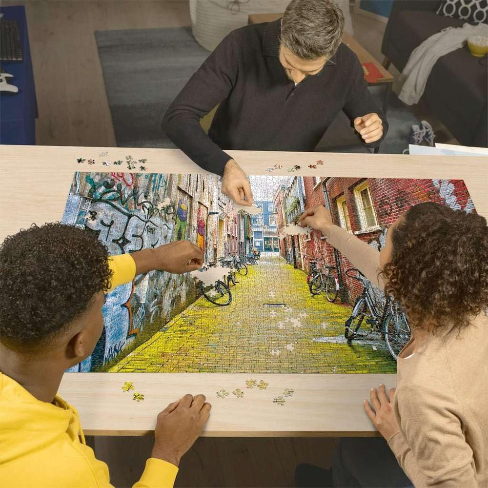 Trois personnes assemblent un puzzle d'une ruelle avec graffitis et vélos.