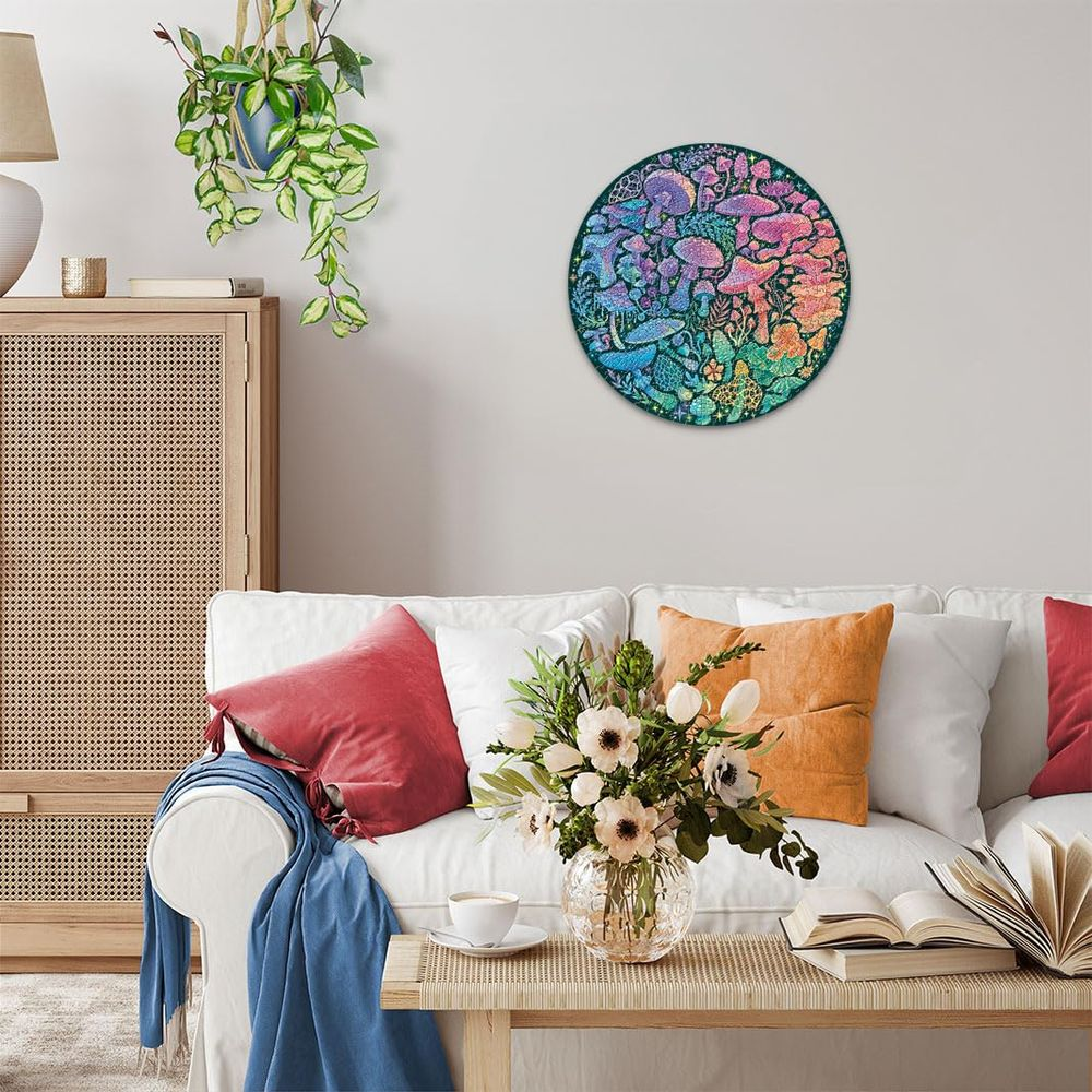 Ein rundes Pilz-Kunstwerk hängt über einem weißen Sofa mit bunten Kissen und einem Strauß.