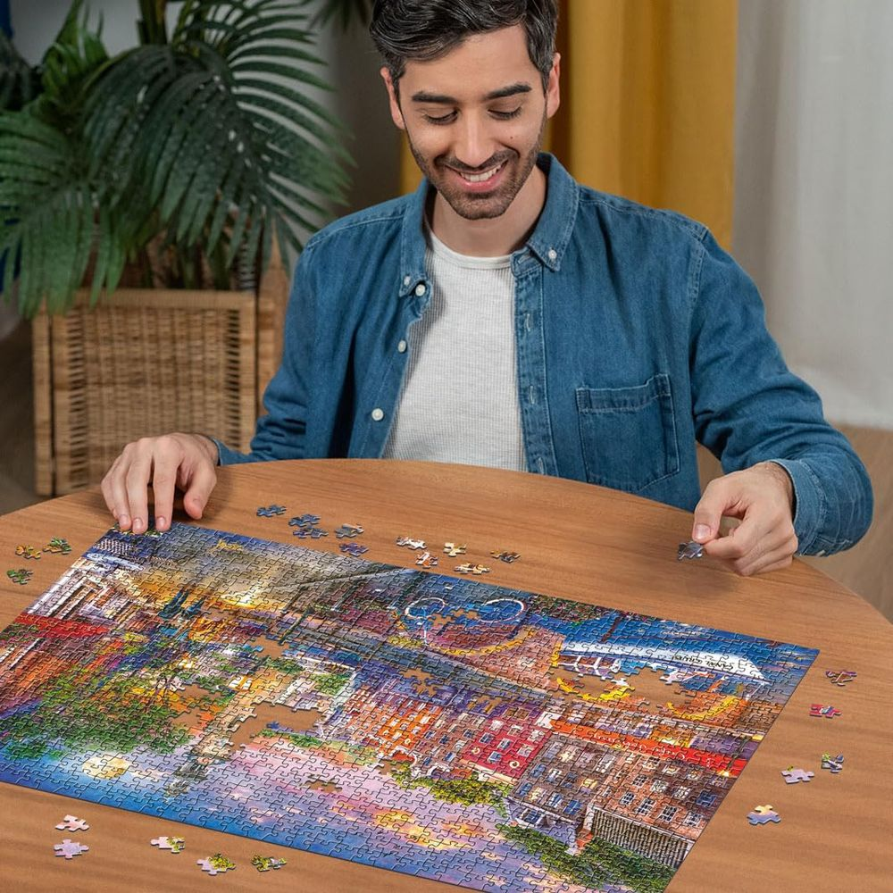 Un homme complète un puzzle représentant une scène de ville nocturne.