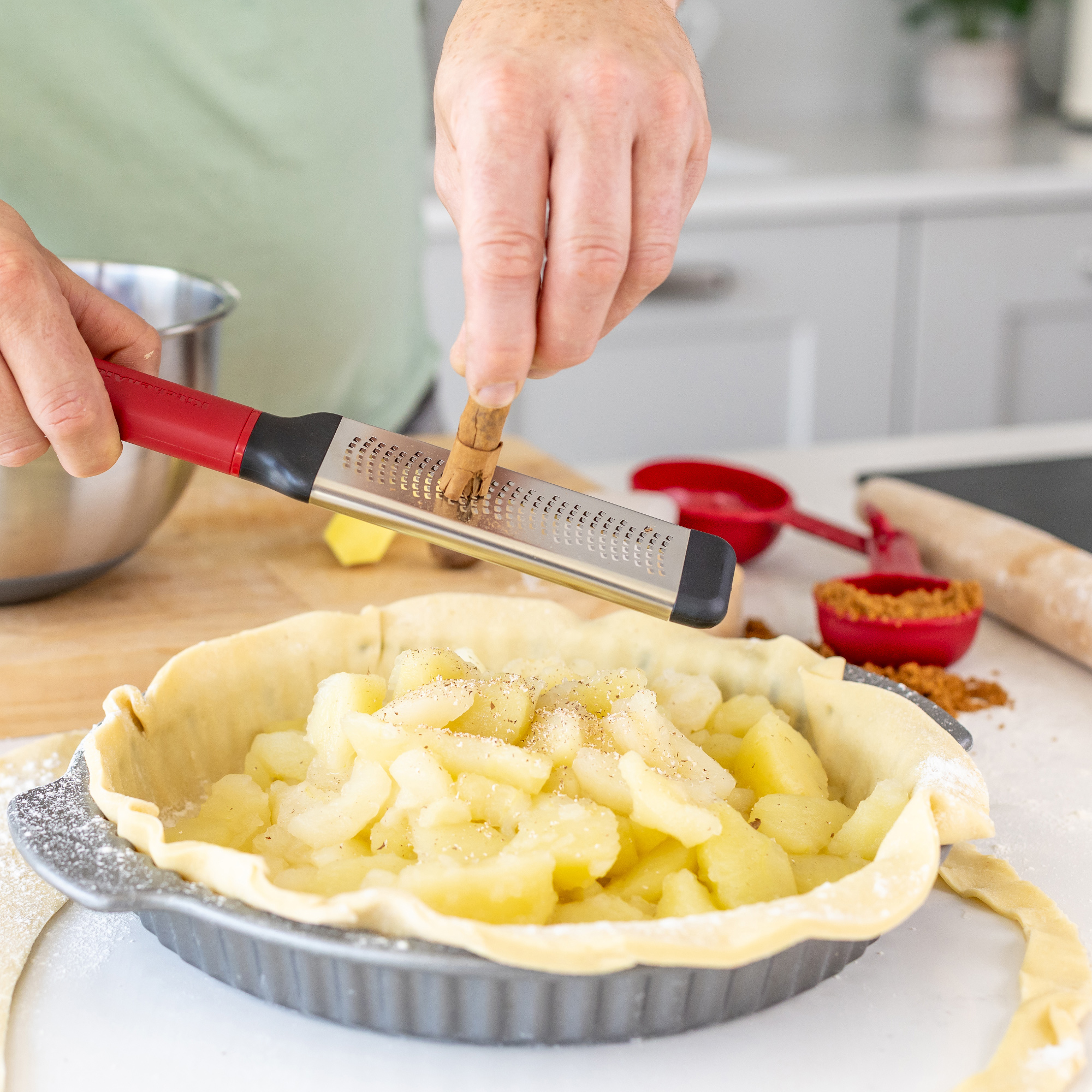 Zimt wird über einen Apfelkuchen mit ungebackener Kruste gerieben.