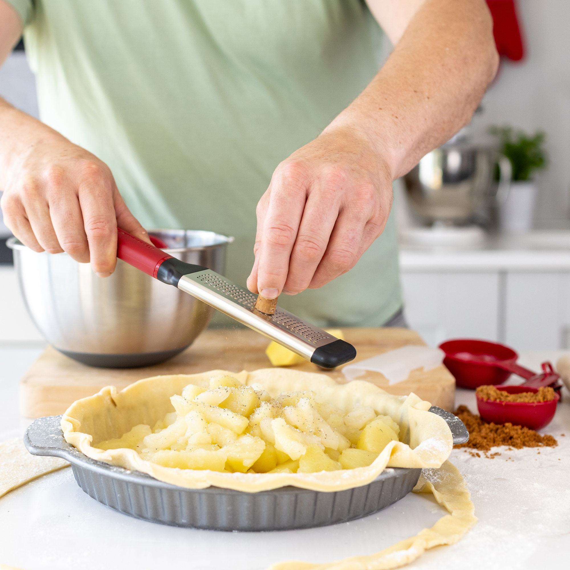 Jemand reibt Muskatnuss über einen Kuchen mit Apfelfüllung.