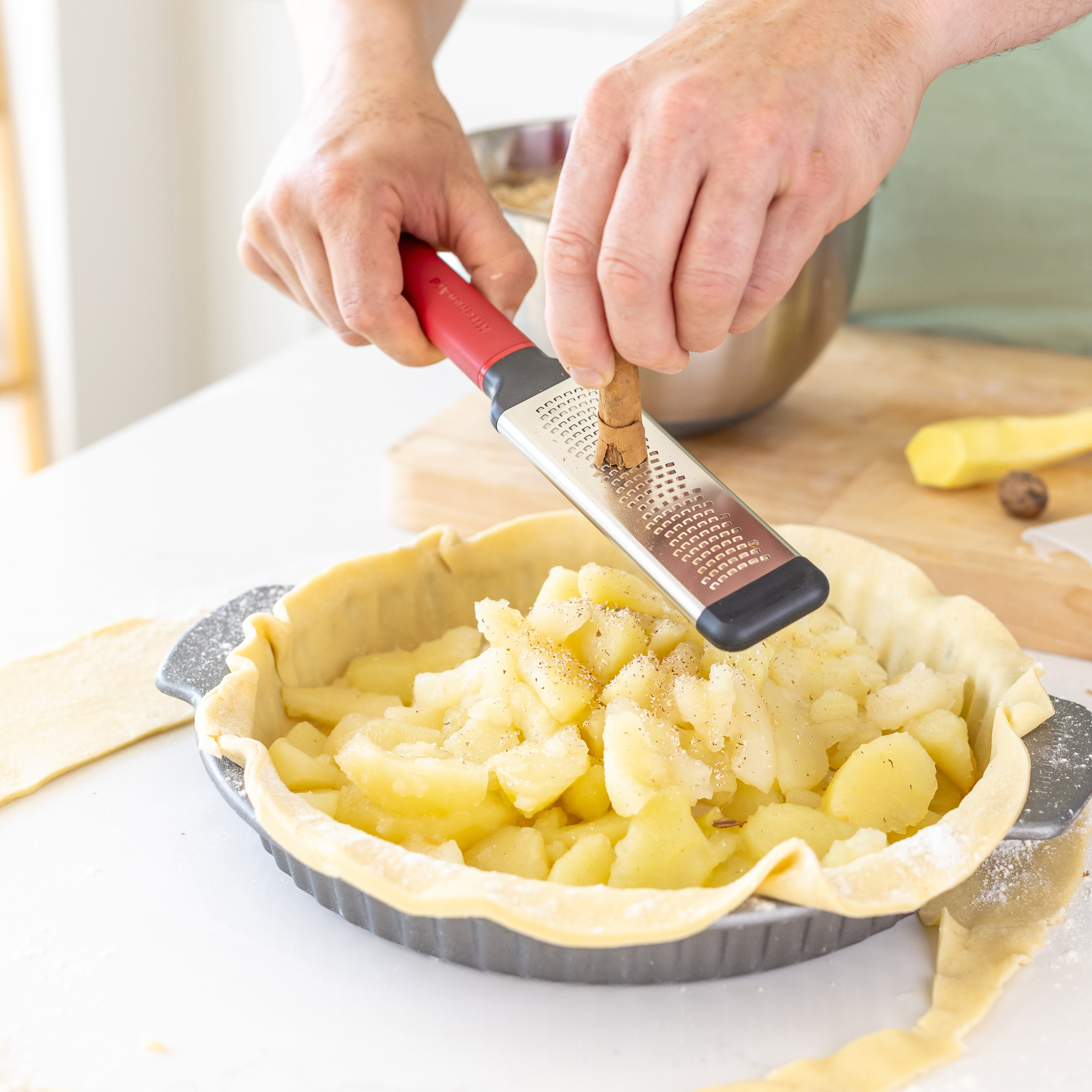Hände reiben Zimt über Apfelfüllung in einer Tarteform.