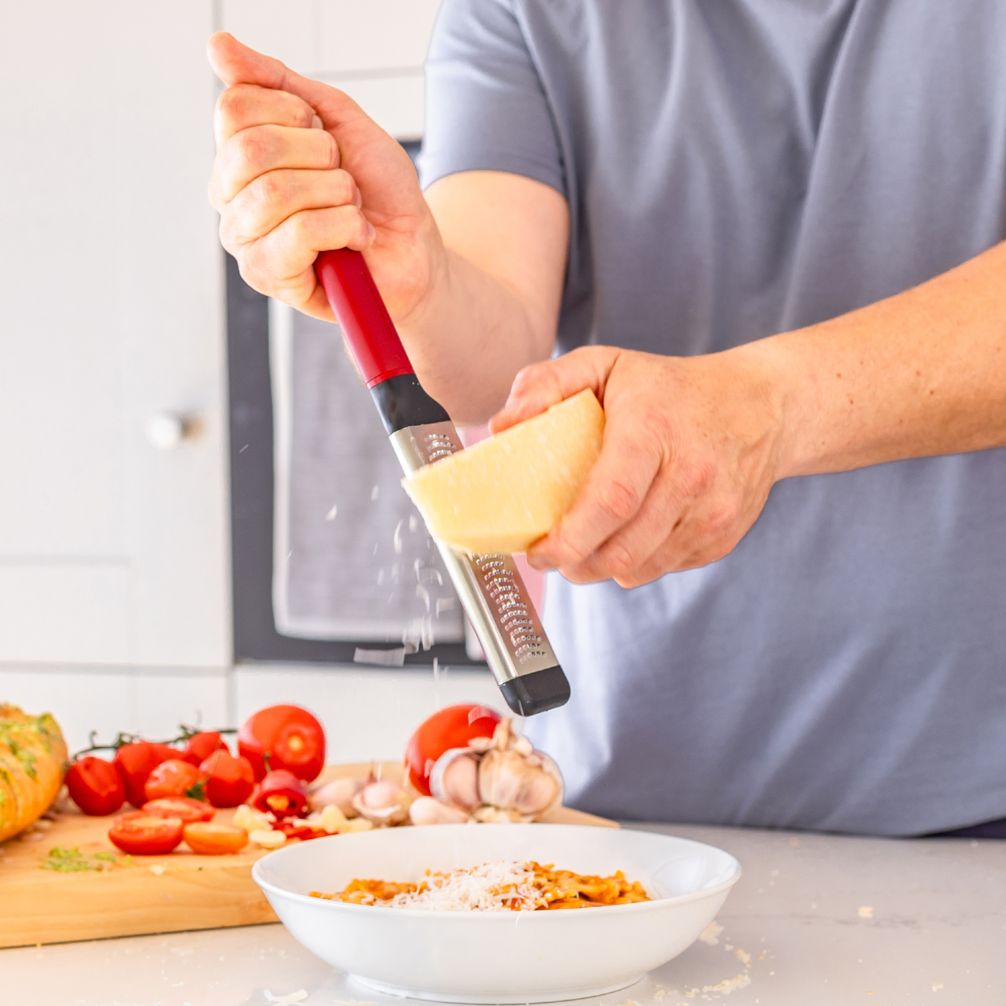 Jemand reibt Käse mit einer Reibe über eine Schüssel Pasta.