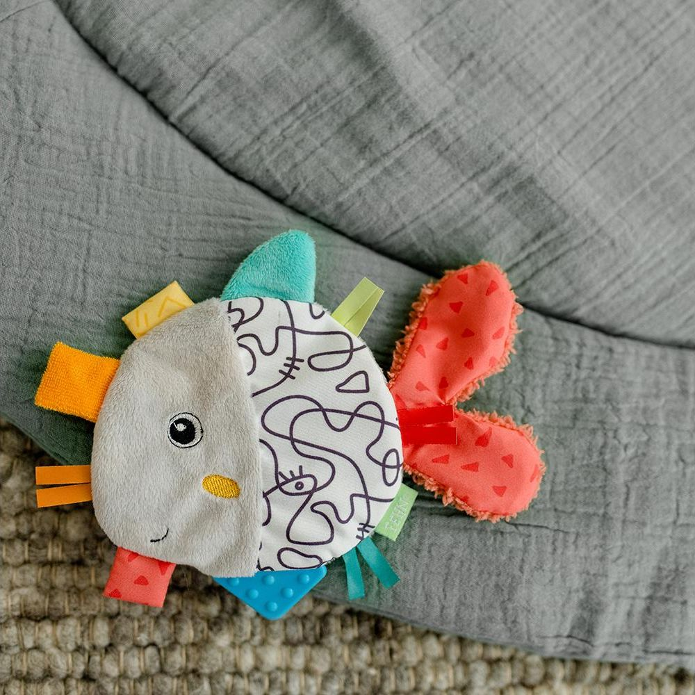 Un giocattolo a forma di pesce in tessuto con texture varie e nastri colorati.