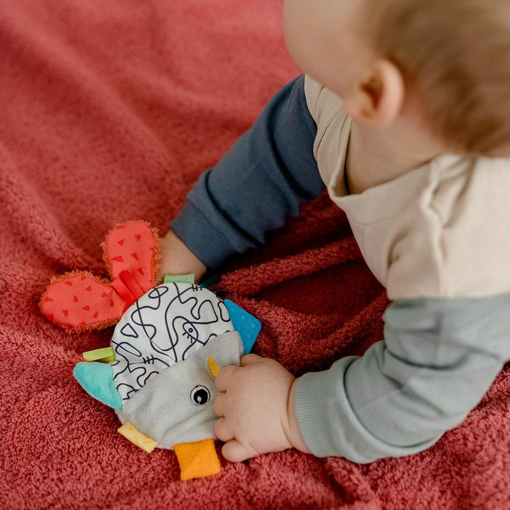 Un bambino è sdraiato su una coperta e gioca con un giocattolo di peluche colorato.
