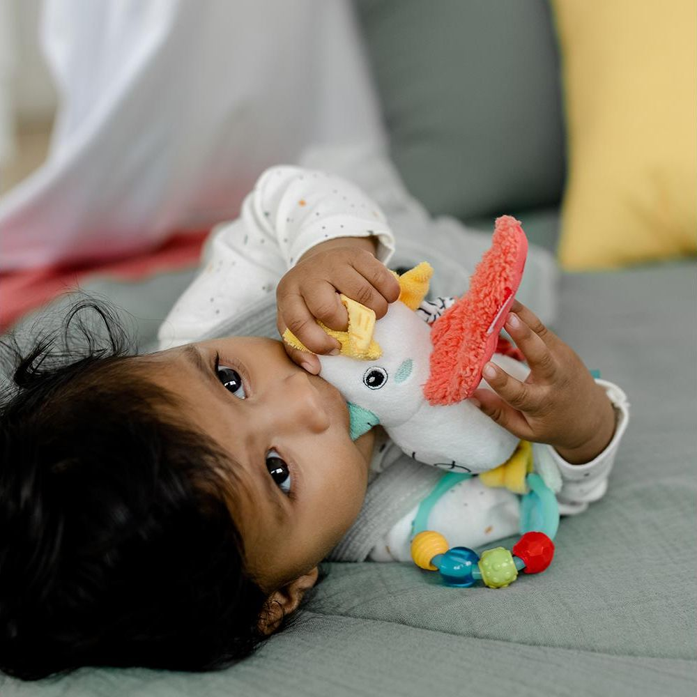 Un bébé est allongé sur le dos jouant avec une licorne en peluche colorée.