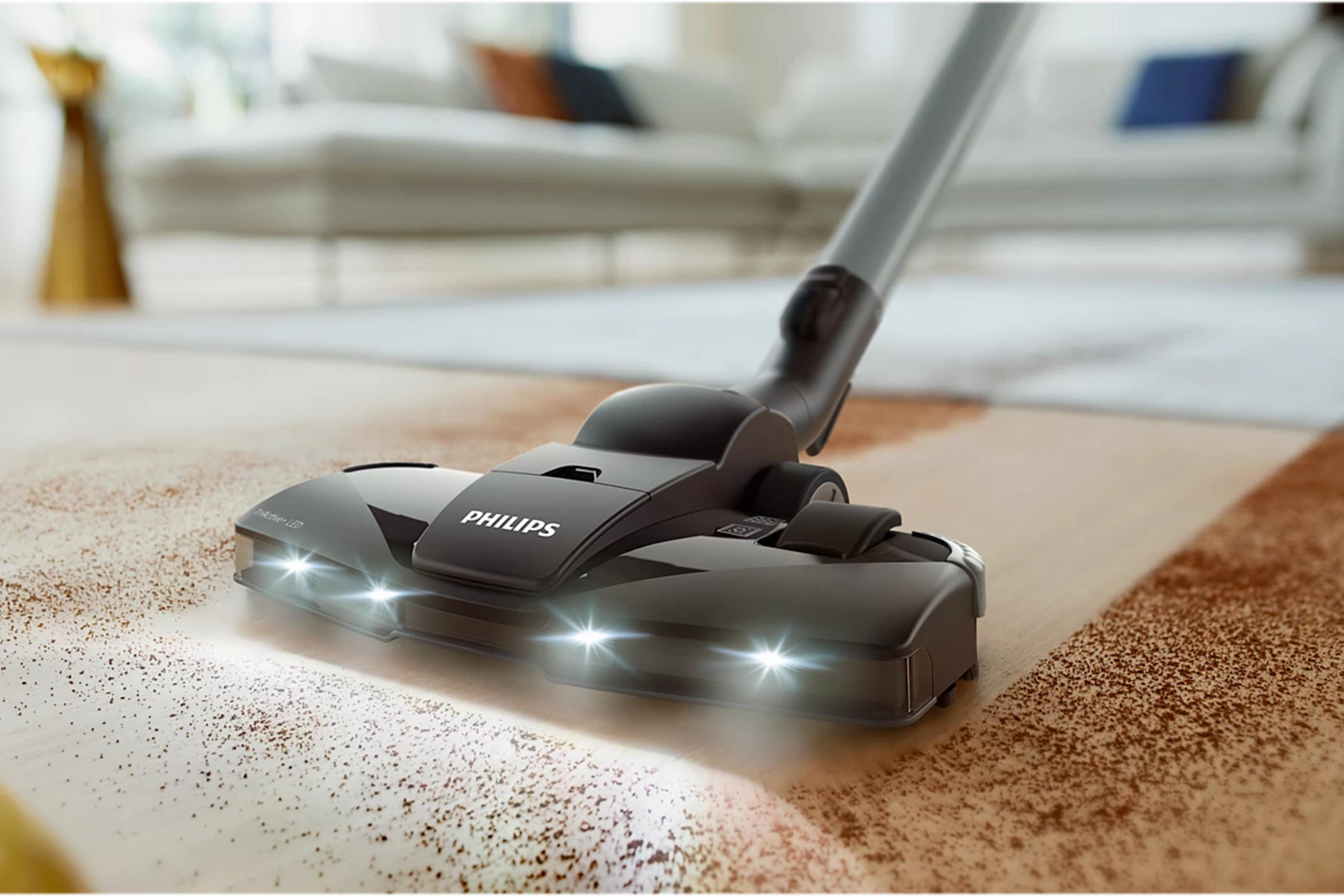 Aspirateur Philips noir avec LED nettoyant un sol en bois poussiéreux.
