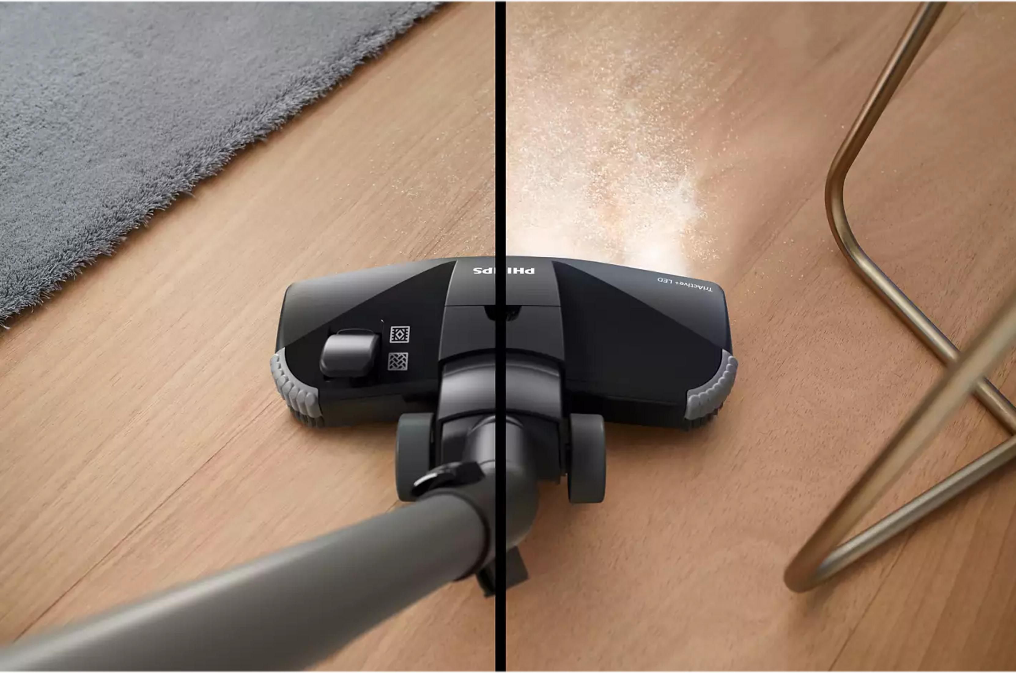 Une tête d'aspirateur nettoie un parquet, la poussière est soulevée.