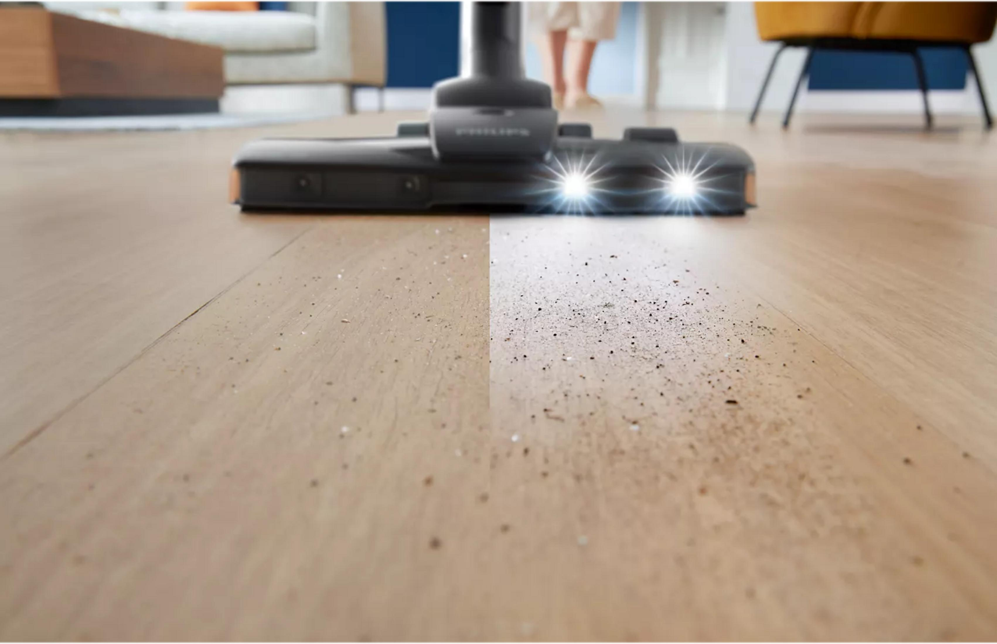 Tête d'aspirateur sur parquet, lumières éclairant la saleté.