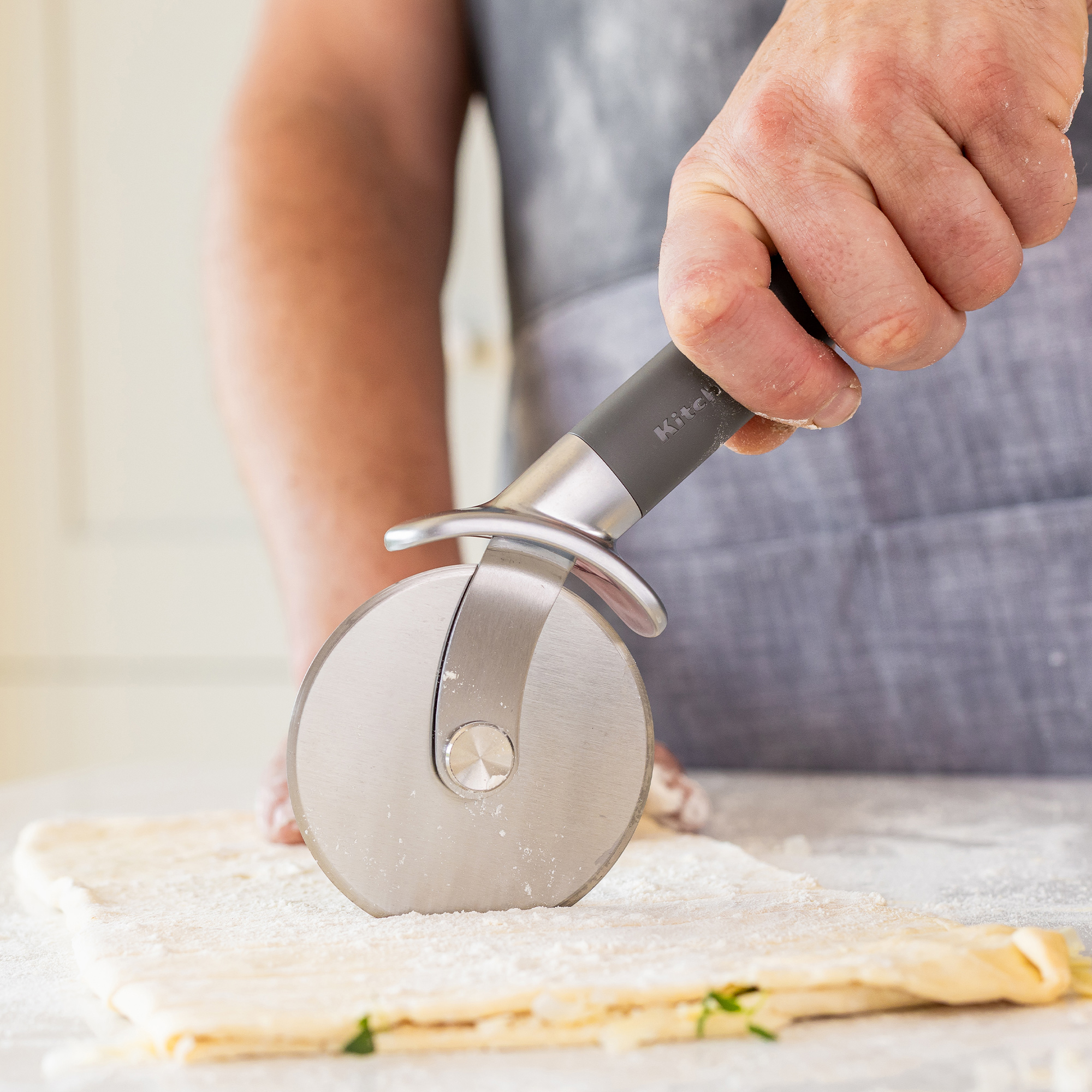 Eine Hand benutzt ein Pizzarad, um Teig zu schneiden. Mehl liegt auf dem Teig.