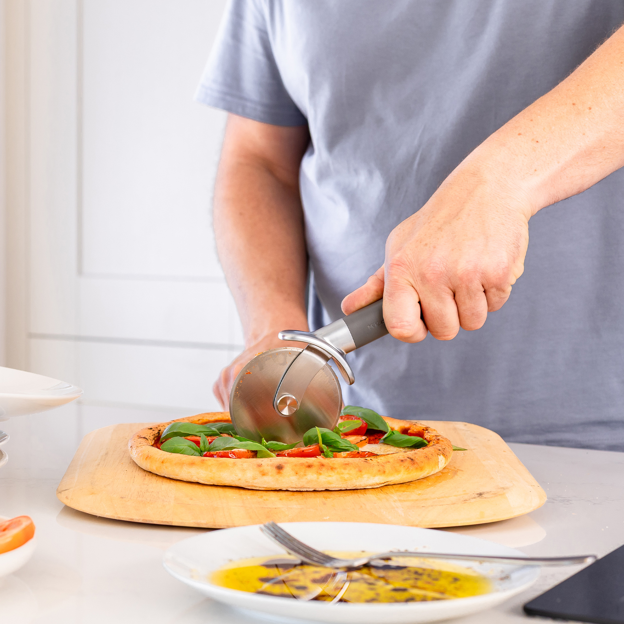 Ein Mann schneidet eine Pizza mit Tomaten und Basilikum mit einem Pizzaschneider.