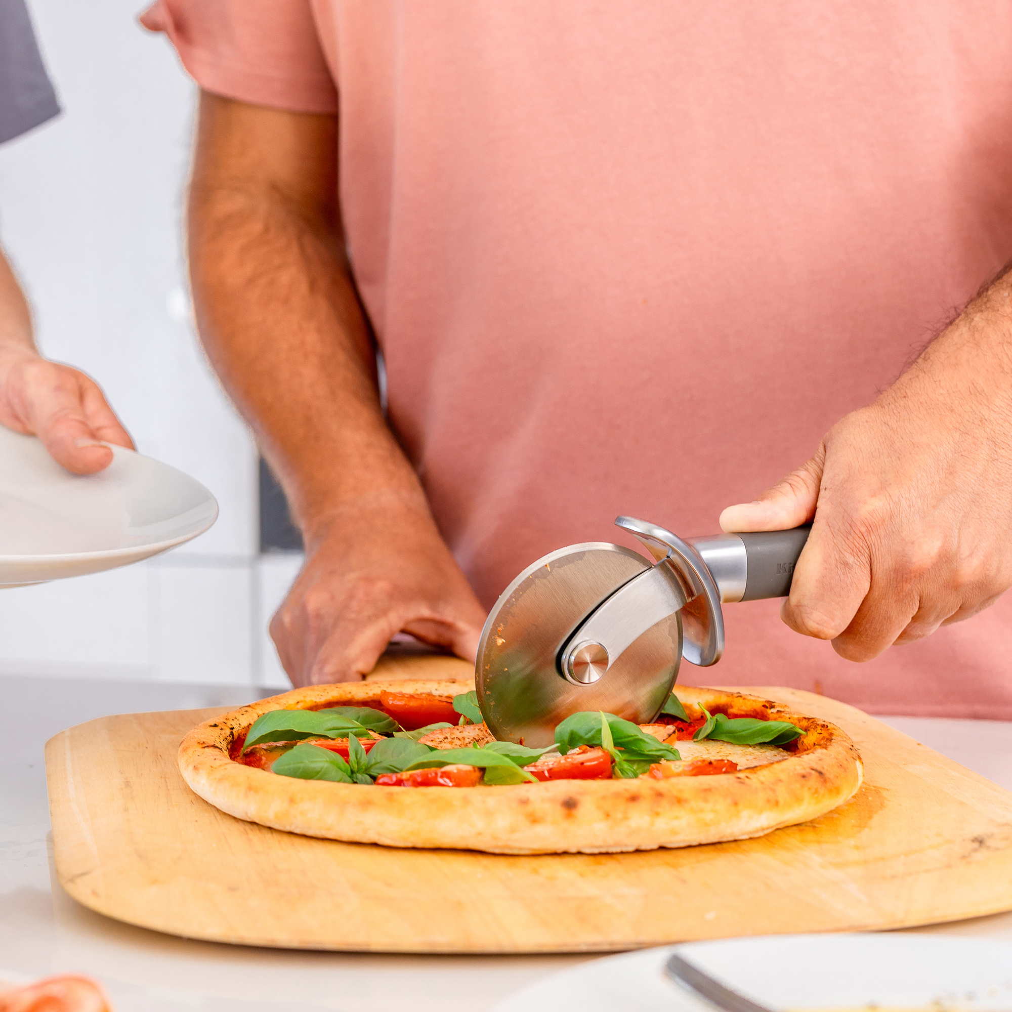 Eine Person schneidet eine Pizza mit Tomaten und Basilikum mit einem Pizzaschneider.