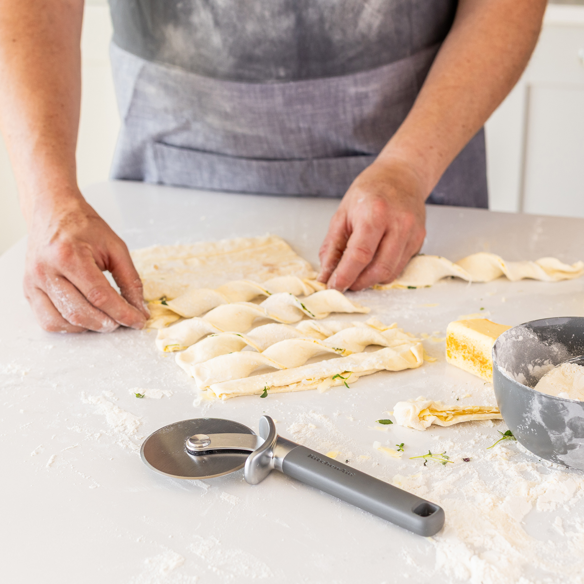 Hände formen Blätterteig auf einer bemehlten Arbeitsfläche neben einem Pizzaschneider.