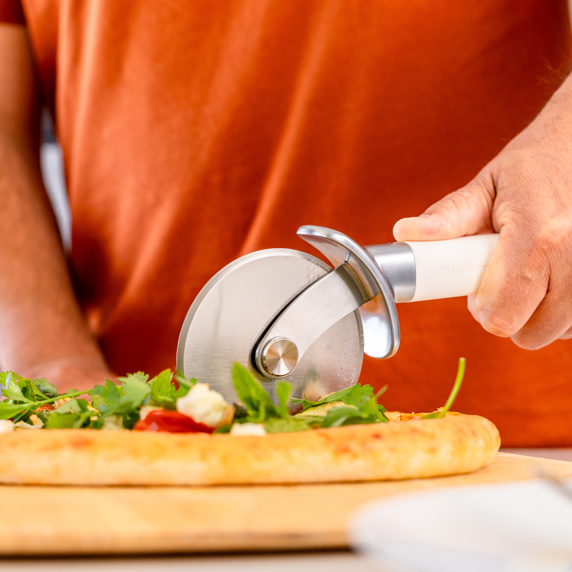 Ein Pizzaschneider schneidet eine Pizza mit Belag aus Kräutern und Käse.