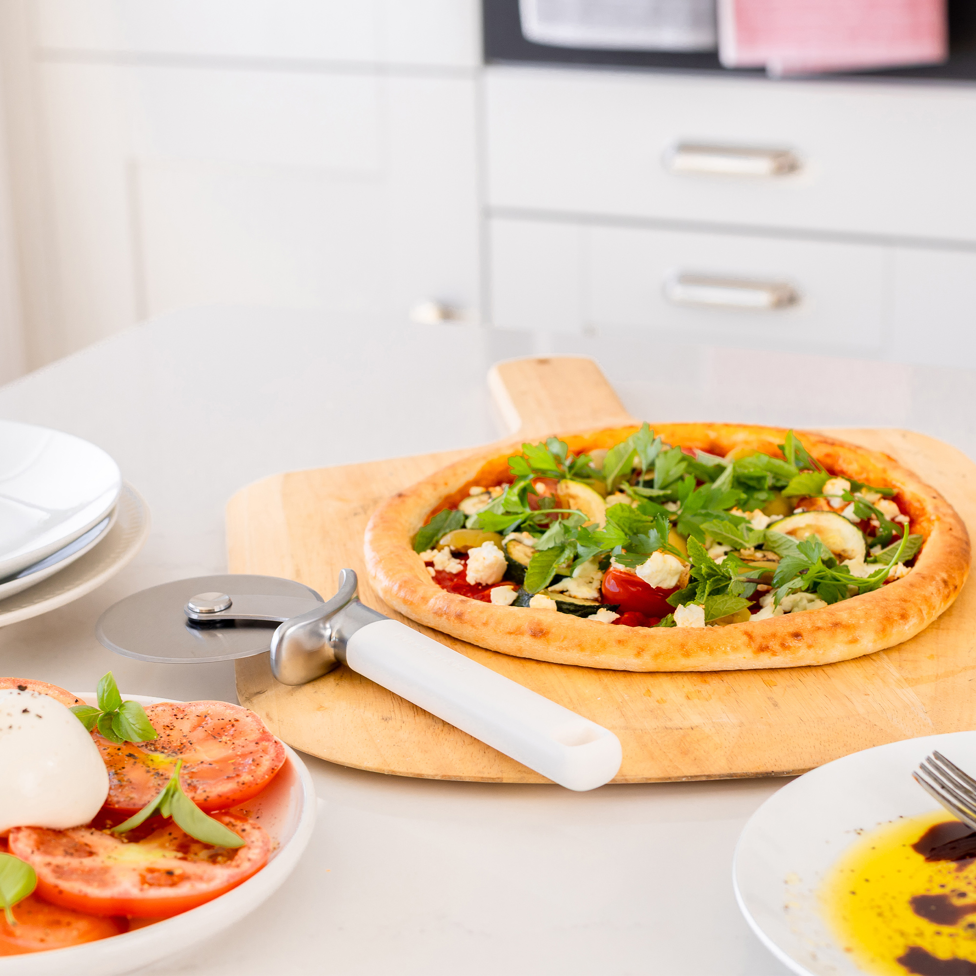 Ein Gemüsepizza mit Tomaten, Zucchini und Feta auf einem Holzbrett.