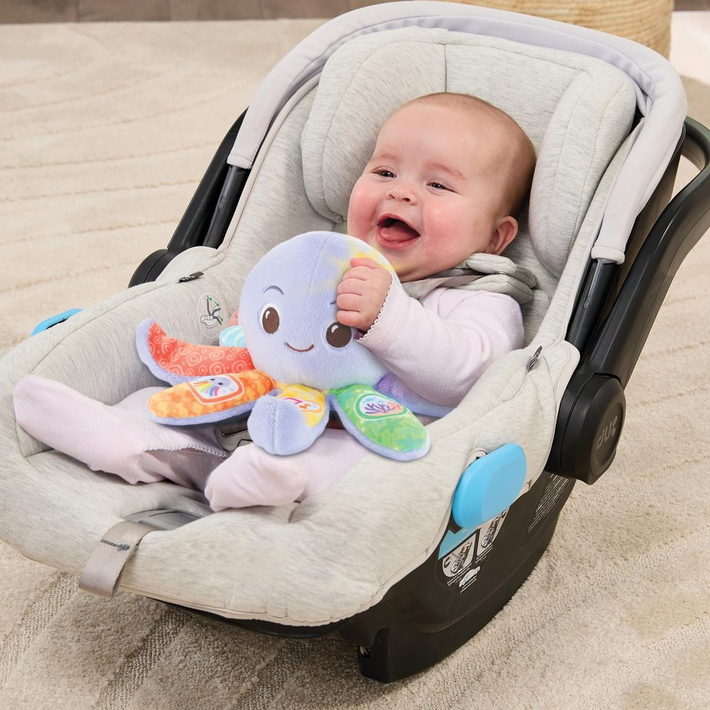 Un bambino ride tenendo un peluche polpo colorato in un seggiolino auto.