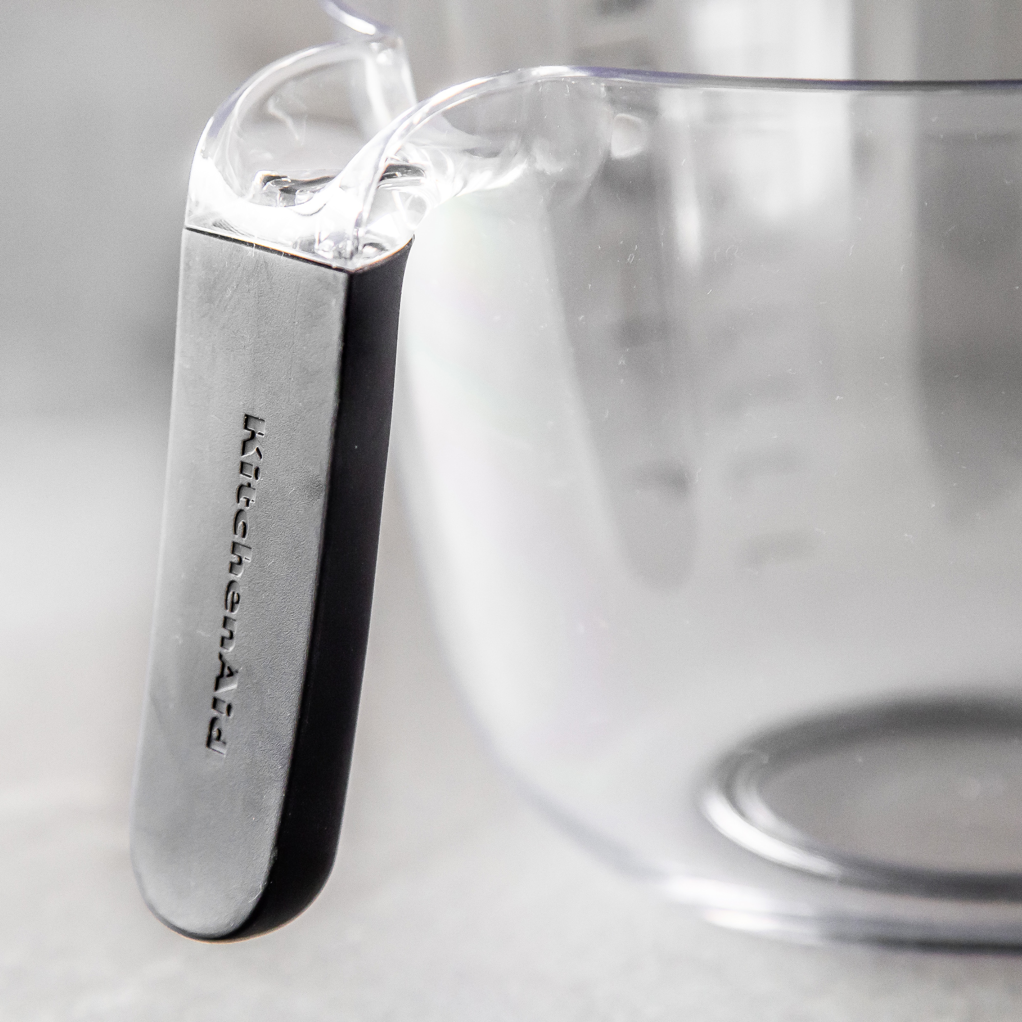 Ein klarer Messbecher mit schwarzem Griff und KitchenAid-Logo.