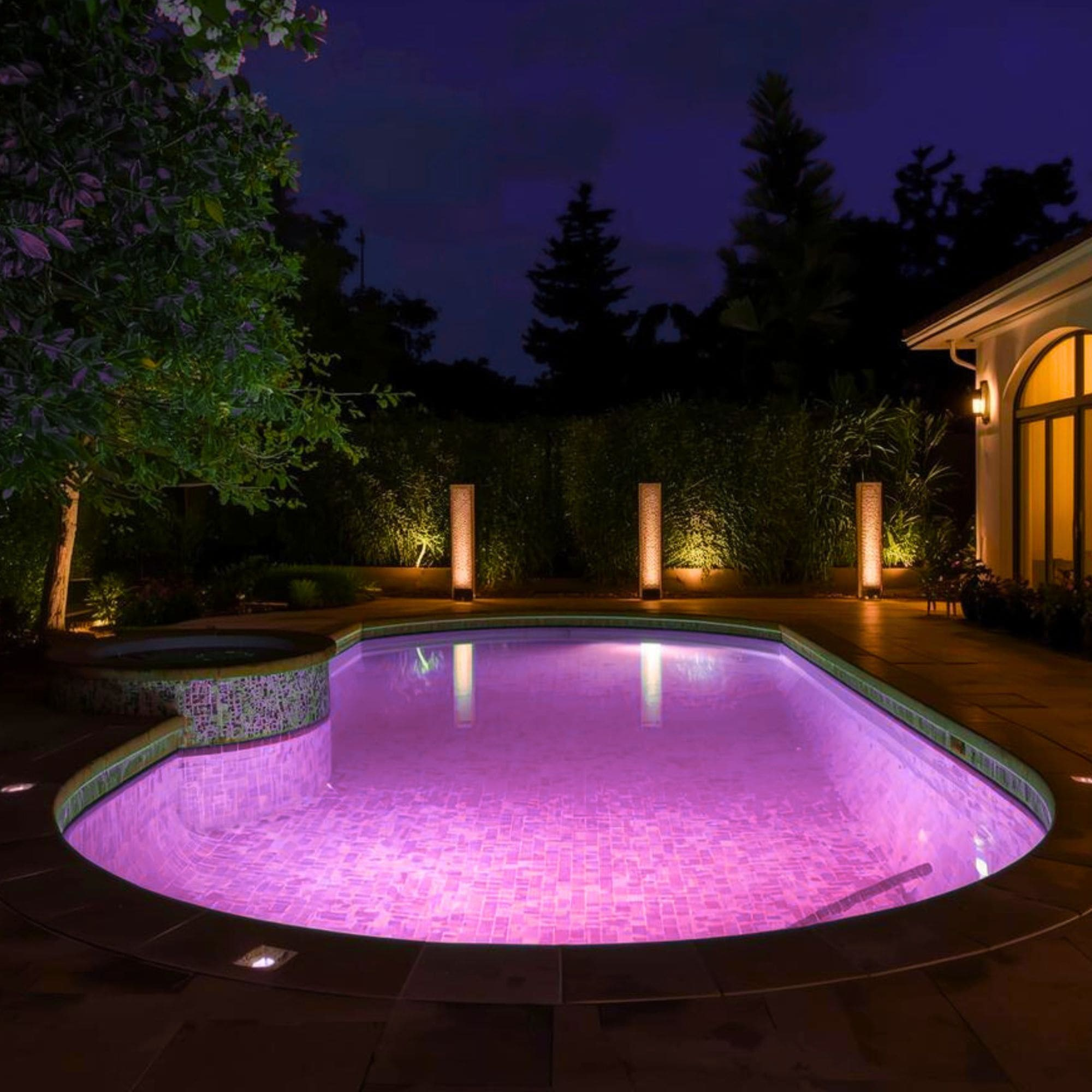 Una piscina iluminada con luz morada, rodeada de árboles y una casa de noche.