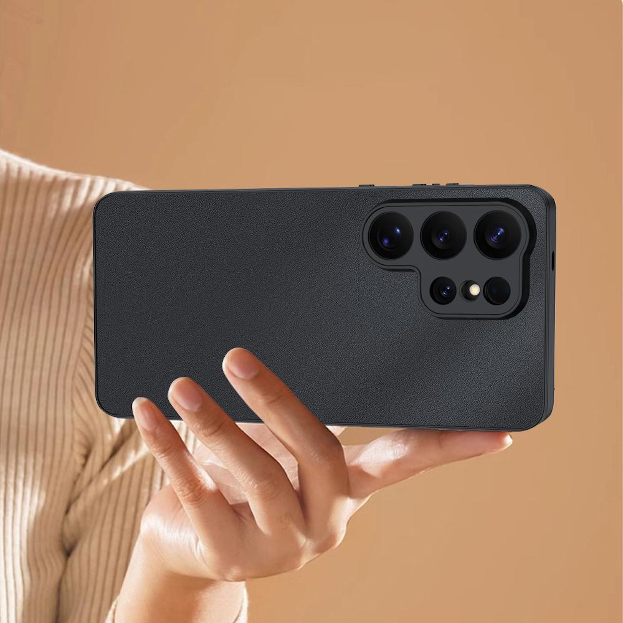 Una mano sostiene un smartphone negro con un módulo de cámara prominente. El fondo es beige.